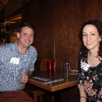 Two alumni sitting at a table smiling for camera
